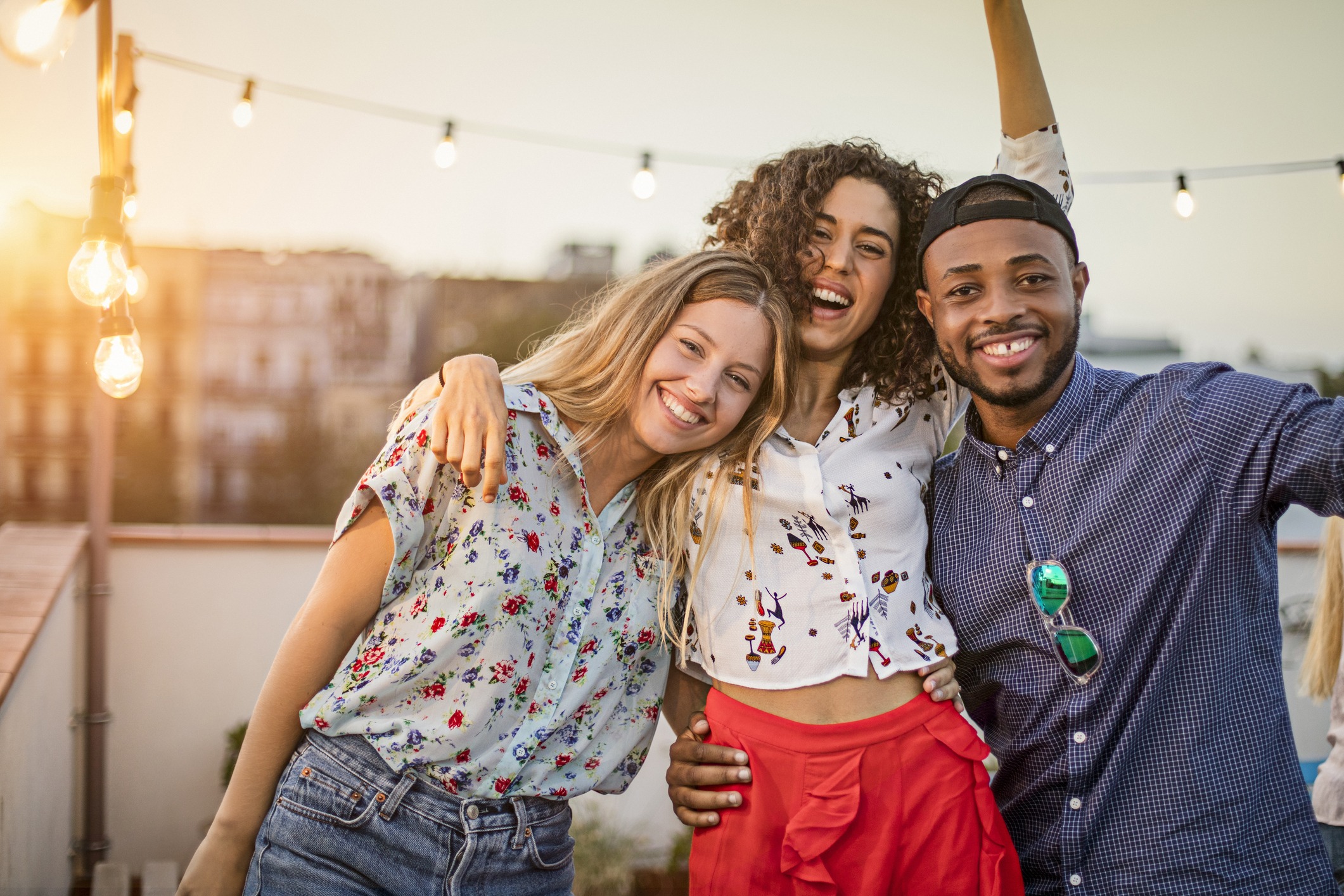 Portrait of happy multi ethnic friends enjoying on terrace. Smiling man and women are celebrating together during sunset. They are wearing casuals in party.